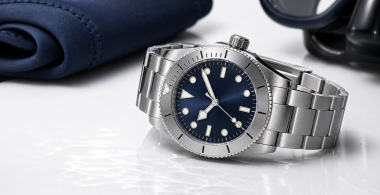 A stainless-steel dive watch beside a map, diving mask, and folded fabric strap