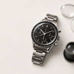 Omega Speedmaster Professional: Models, References and Buying Guide Steel chronograph watch beside a loupe and blank reference card for a buying guide